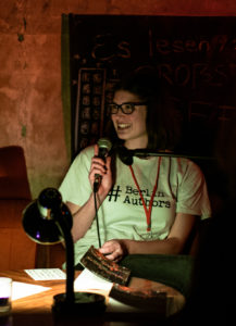 Teammitglied Liv: Braunhaarige Frau mit Brille, Anfang Zwanzig, sitzt an einem Tisch und spricht lächelnd in ein Mikrofon