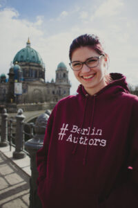 Frau mit braunen Haaren und rotem Pulli steht vor dem Berliner Dom.